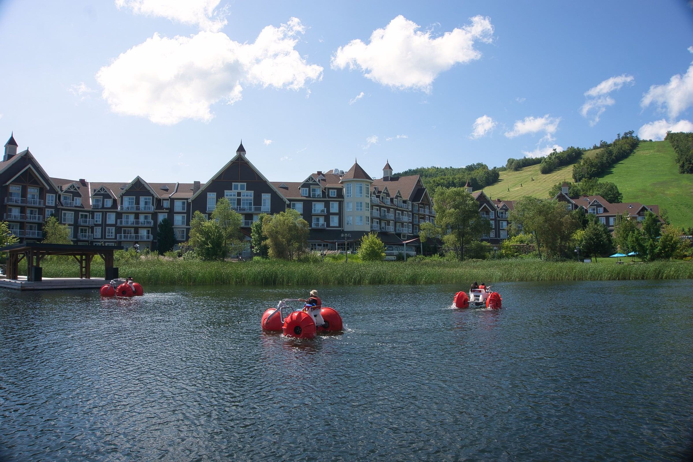 Water trikes on Mill Pond in front of Blue Mountain Village with green ski slopes behind