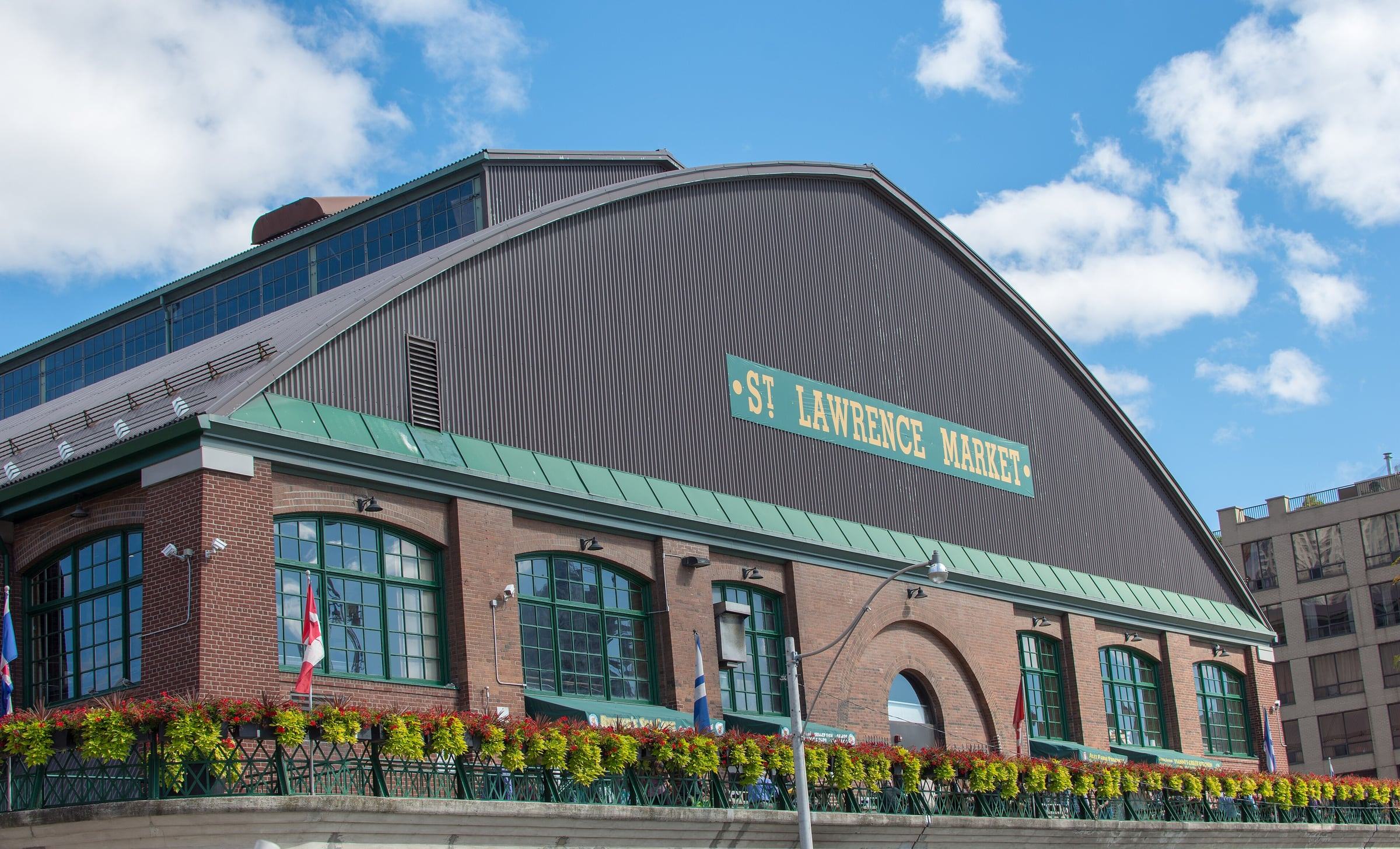 Brick facade of St. Lawrence Market with its green sign, arched windows and hanging flower baskets