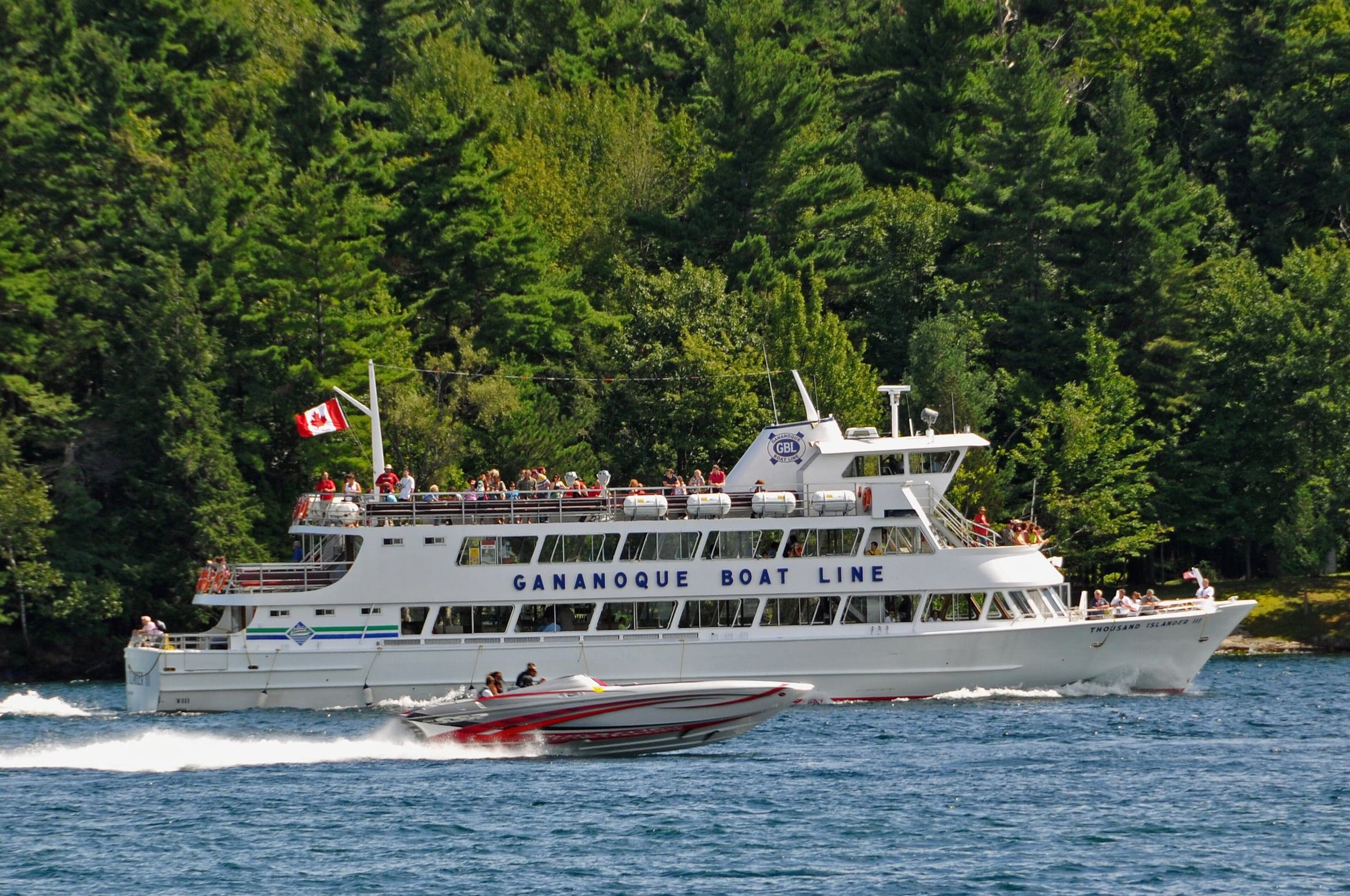 Gananoque Boat Line cruise ship with passengers on deck passing a forested Thousand Islands shore